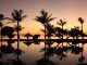 Bild eines Urlaubsortes bei Sonnenuntergang. Palmen und Sonnenschirme spiegeln sich im Wasser